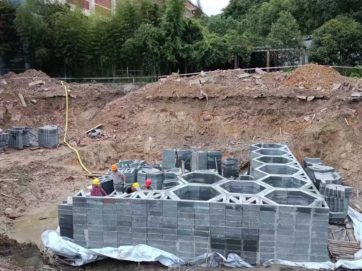 工地深基坑内，建筑工人正在基坑内拼装垒筑蜂巢状硅砂雨水收集池模块