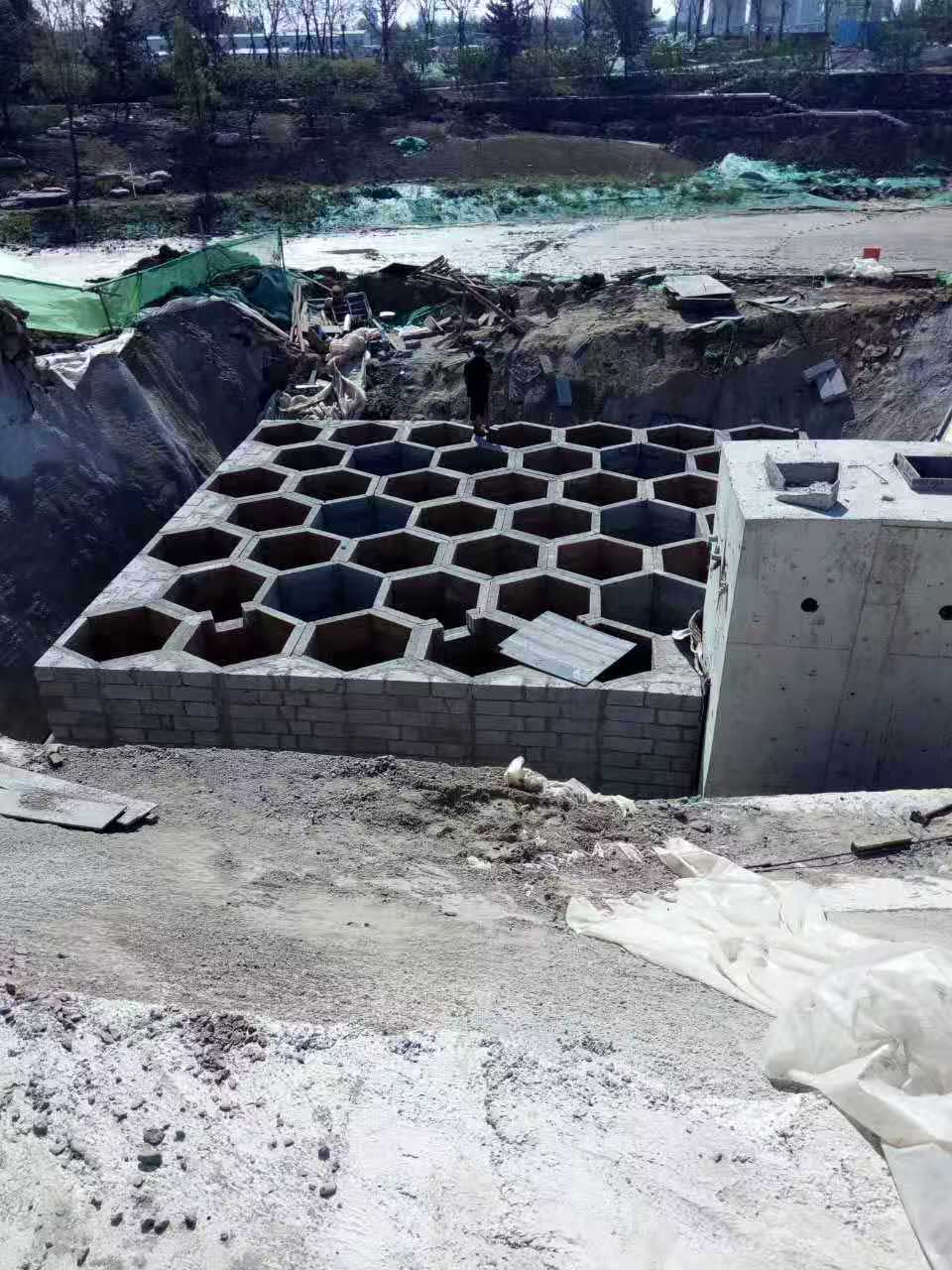 大型地下硅砂雨水收集池，展现大面积壮观且规整的六边形蜂巢网格构造与相邻的混凝土泵房