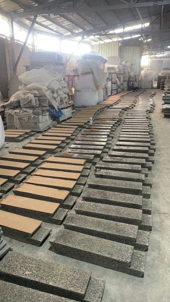 建筑材料工厂车间内，地面上整齐排列着多行刚生产出来的双层复合硅砂透水砖