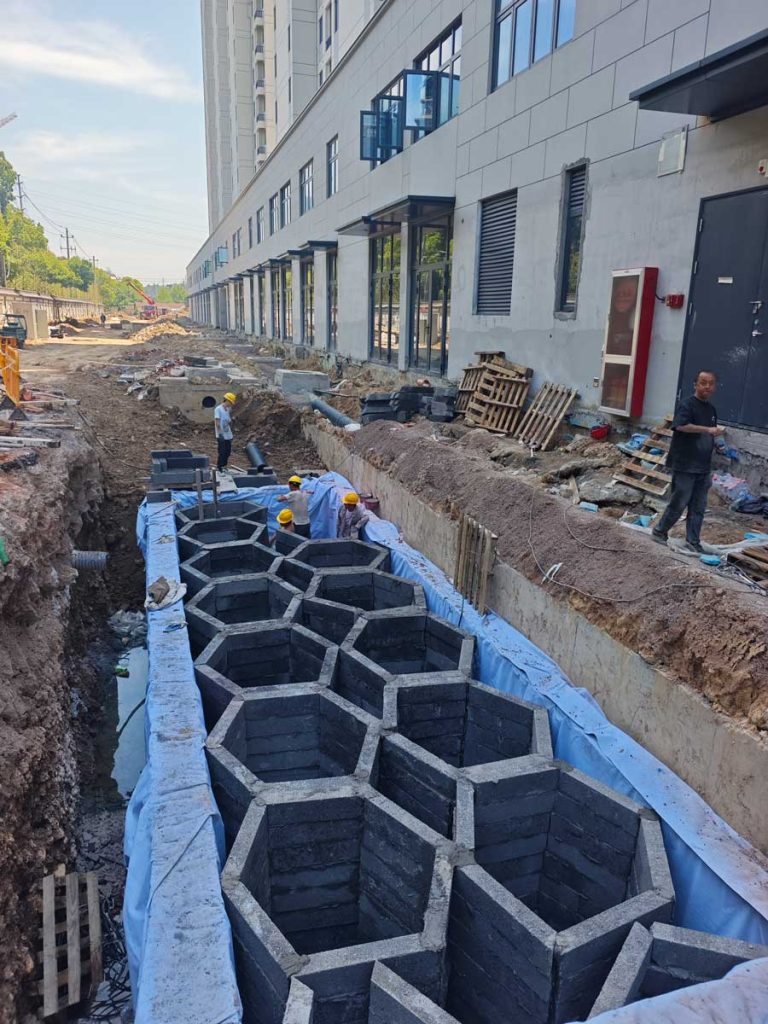 基坑内正在人工砌筑施工的地下狭长形硅砂雨水收集池，展现了连续六边形蜂巢式网格内部结构