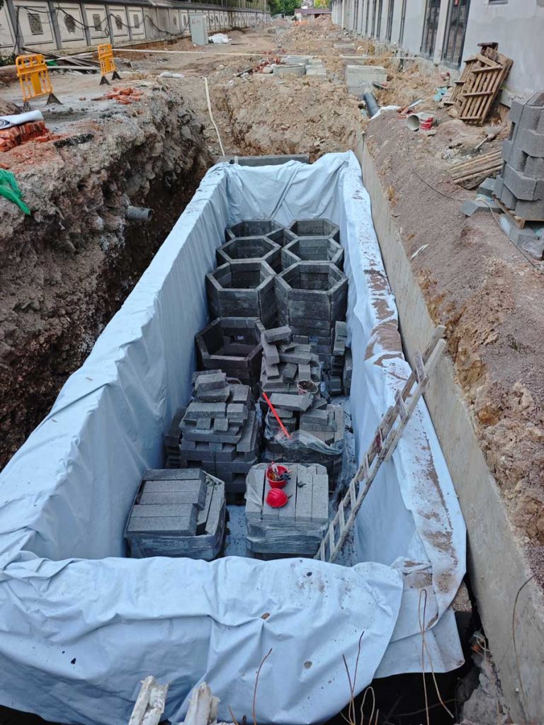 基坑内整体铺满灰白色防渗土工布,远端已垒砌出几个规整的深灰色正六边形蜂巢状蓄水网格