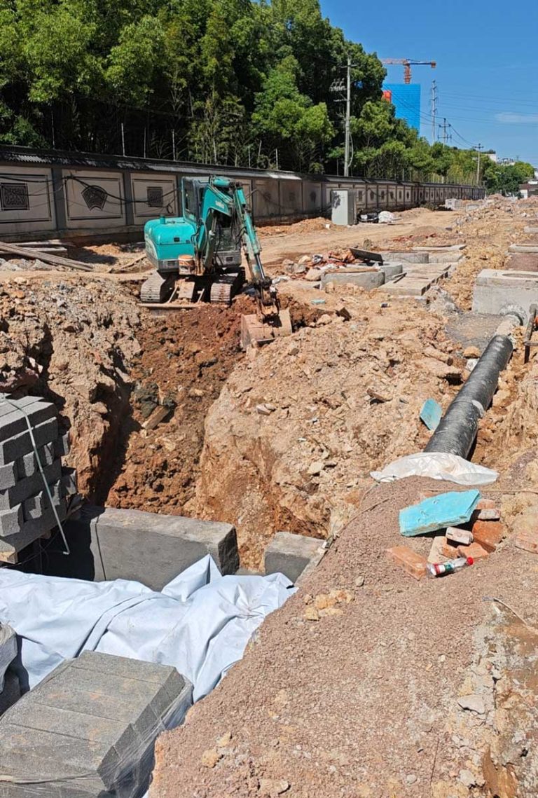 硅砂雨水收集池施工现场,小型挖掘机正在泥土基坑旁进行开挖与地下管网铺设作业