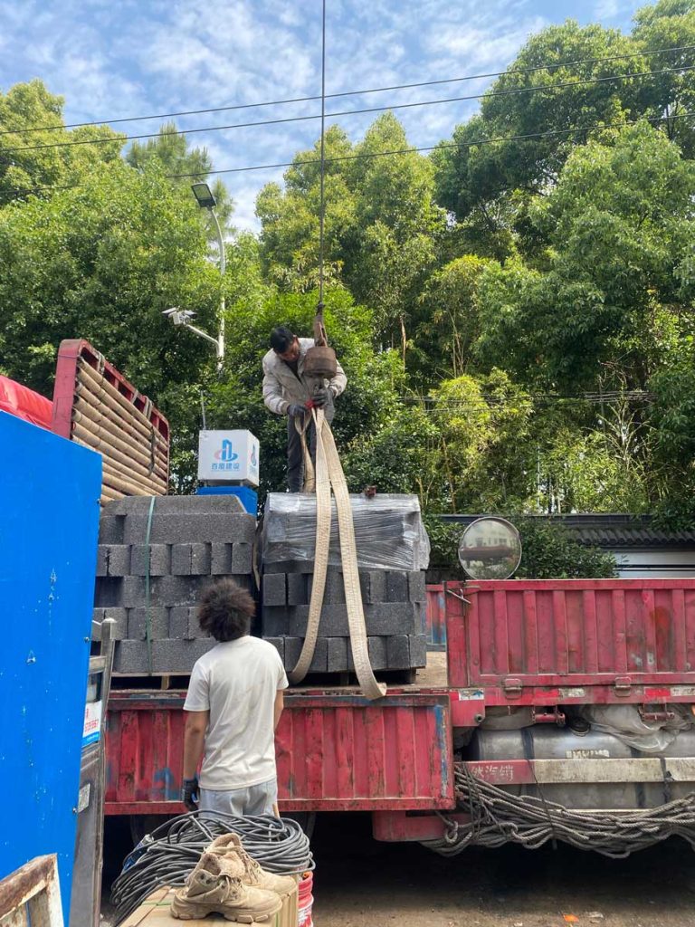 建筑施工现场,一辆装满灰色硅砂雨水收集池模块的红色平板卡车正在卸货