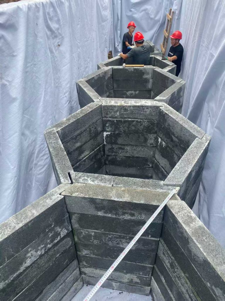 铺满白色防渗土工布的狭长基坑内,工人正在协同拼装正六边形蜂巢状硅砂蓄水井筒