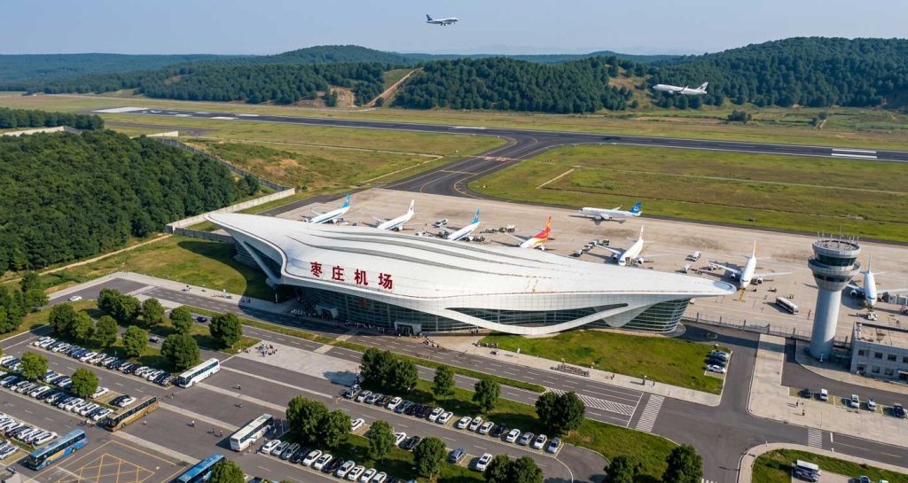 枣庄机场鸟瞰效果图,展现银白色流线型航站楼屋顶、周边绿化带、跑道及塔楼
