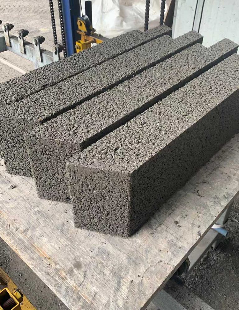 近景特写呈并排摆放的深灰色多孔硅砂砌块，表面具有强烈的透水骨料颗粒质感与拼装切角