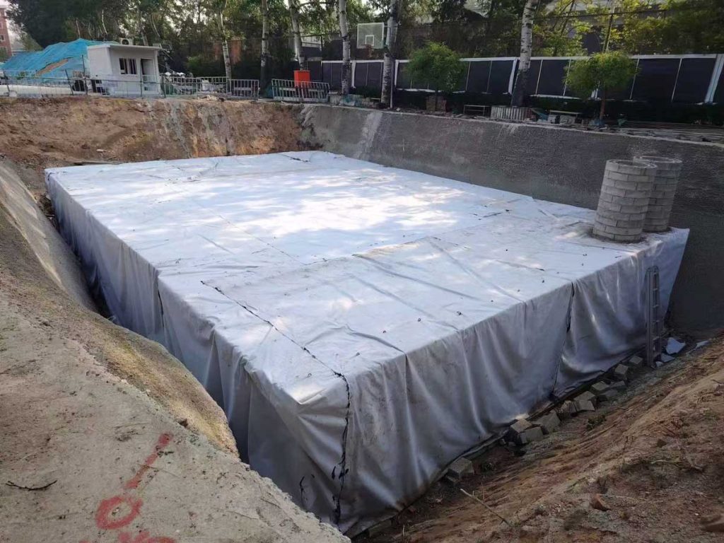 施工现场基坑内,拼装完成并用灰白色土工布整体包裹防渗的硅砂雨水收集池